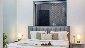 A modern bedroom with a large bed, two bedside tables, a window with a view, and a bedside lamp.
