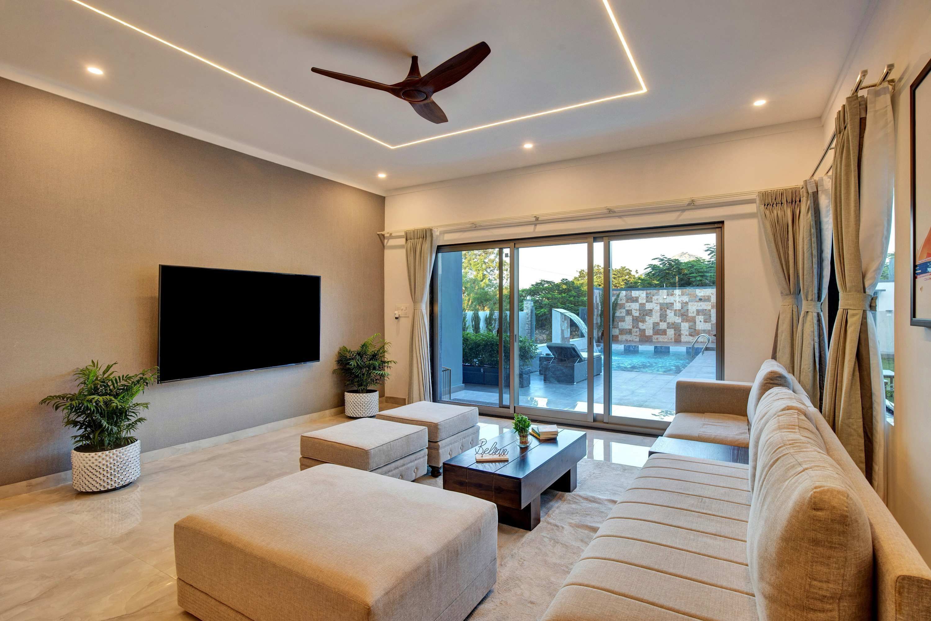 A modern living room with a flat-screen TV, a ceiling fan, and a large sliding glass door leading to an outdoor area.