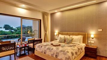 A spacious bedroom with a large bed, a sitting area with a table and chairs, and a balcony with a view of the city.