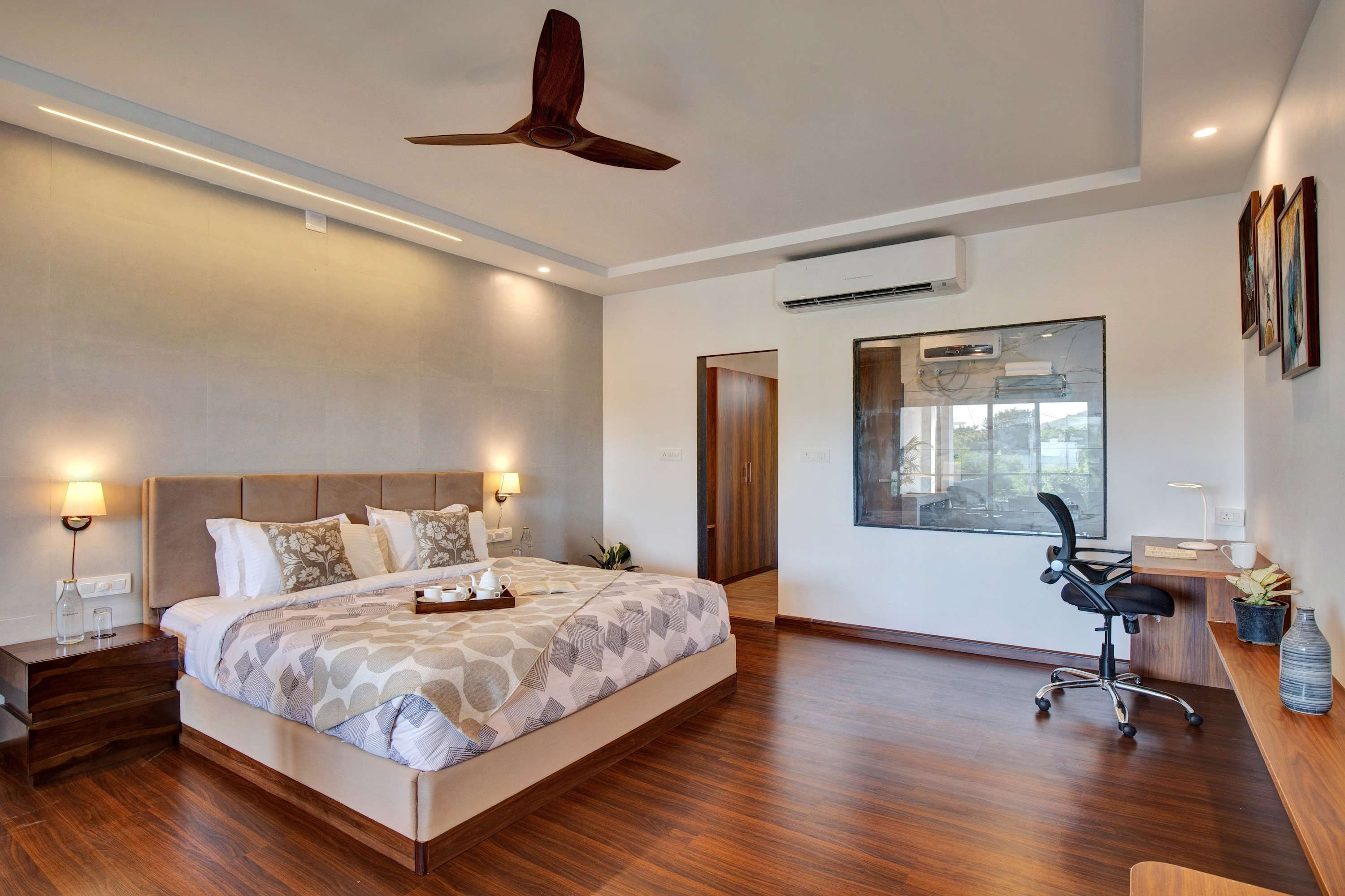 A modern hotel room with a large bed, bedside lamps, an air conditioning unit, a desk with a chair, and a large window.