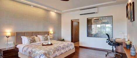 A modern hotel room with a large bed, bedside lamps, an air conditioning unit, a desk with a chair, and a large window.