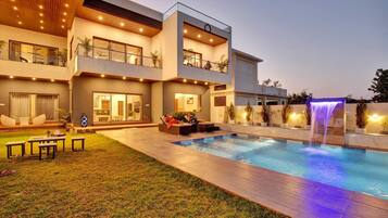 A modern two-story house with a swimming pool and a waterfall feature.