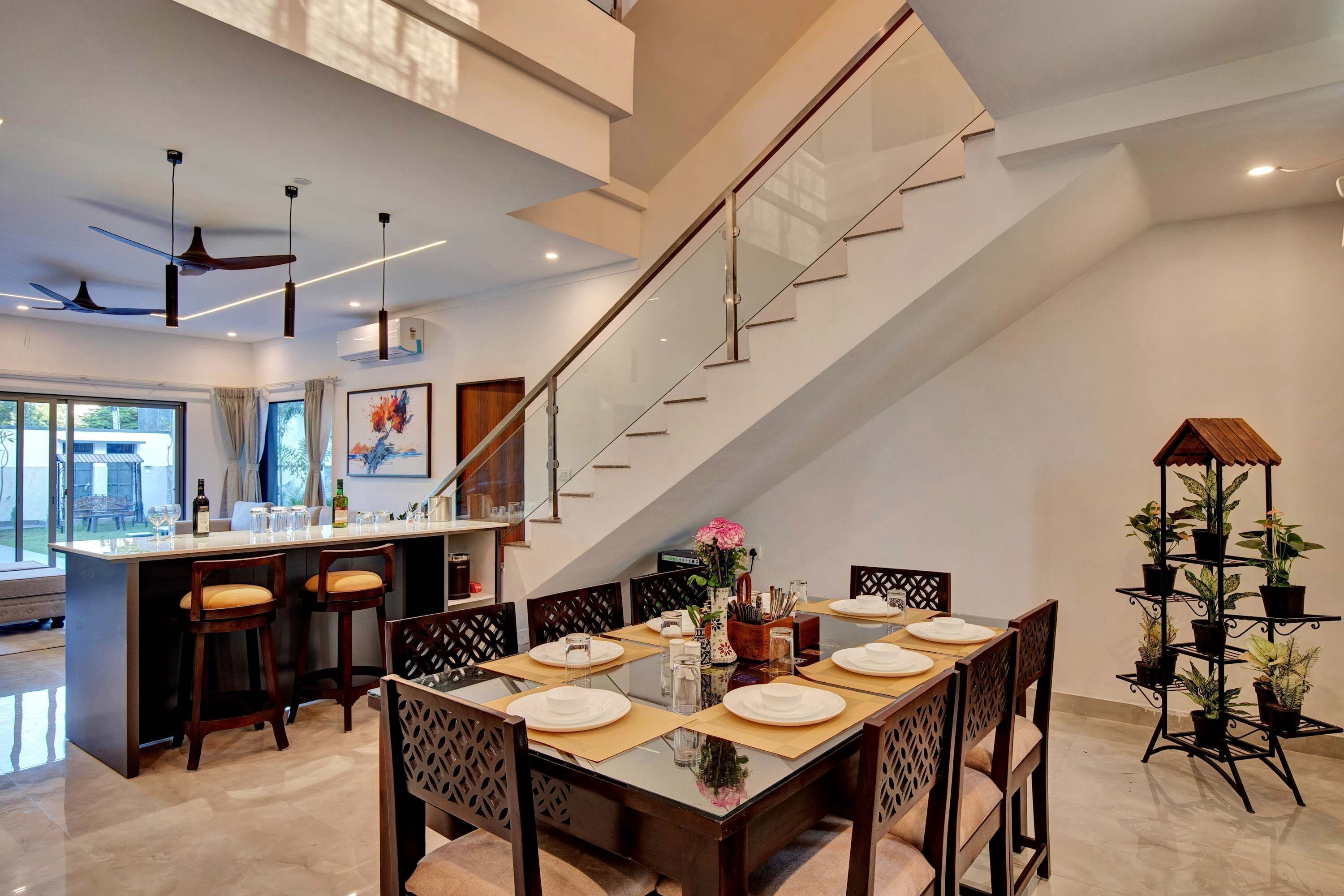 A modern dining area with a glass staircase, a kitchen with bar stools, and a dining table set for four.