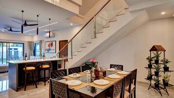 A modern dining area with a glass staircase, a kitchen with bar stools, and a dining table set for four.