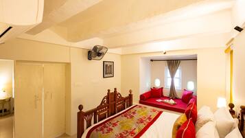 A bedroom with a bed, a wooden chair, a bedside table, a wall-mounted fan, and a window with curtains.