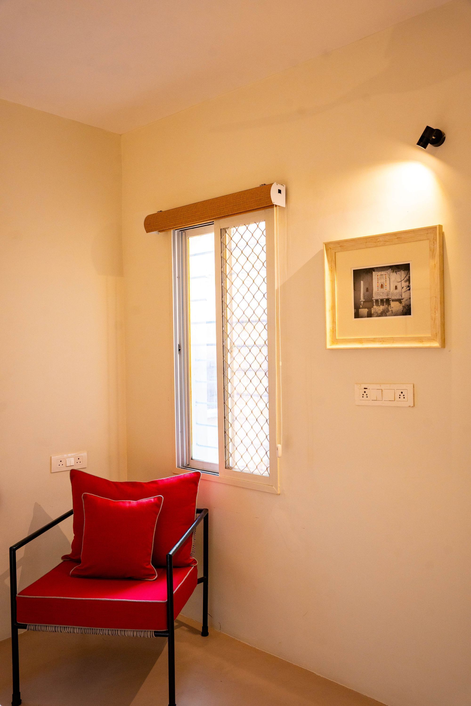 A room with a window, a framed picture on the wall, and a red chair.
