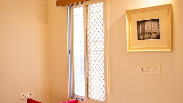 Une pièce avec une fenêtre, un tableau encadré au mur et une chaise rouge.