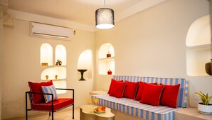 Un salon moderne comprenant un canapé, un fauteuil, une petite table ronde avec un panier de fruits et des appliques murales décoratives.