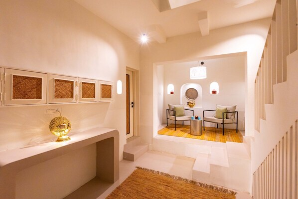 A modern interior with a white console table, a decorative golden object, a seating area with a round table, and a staircase.
