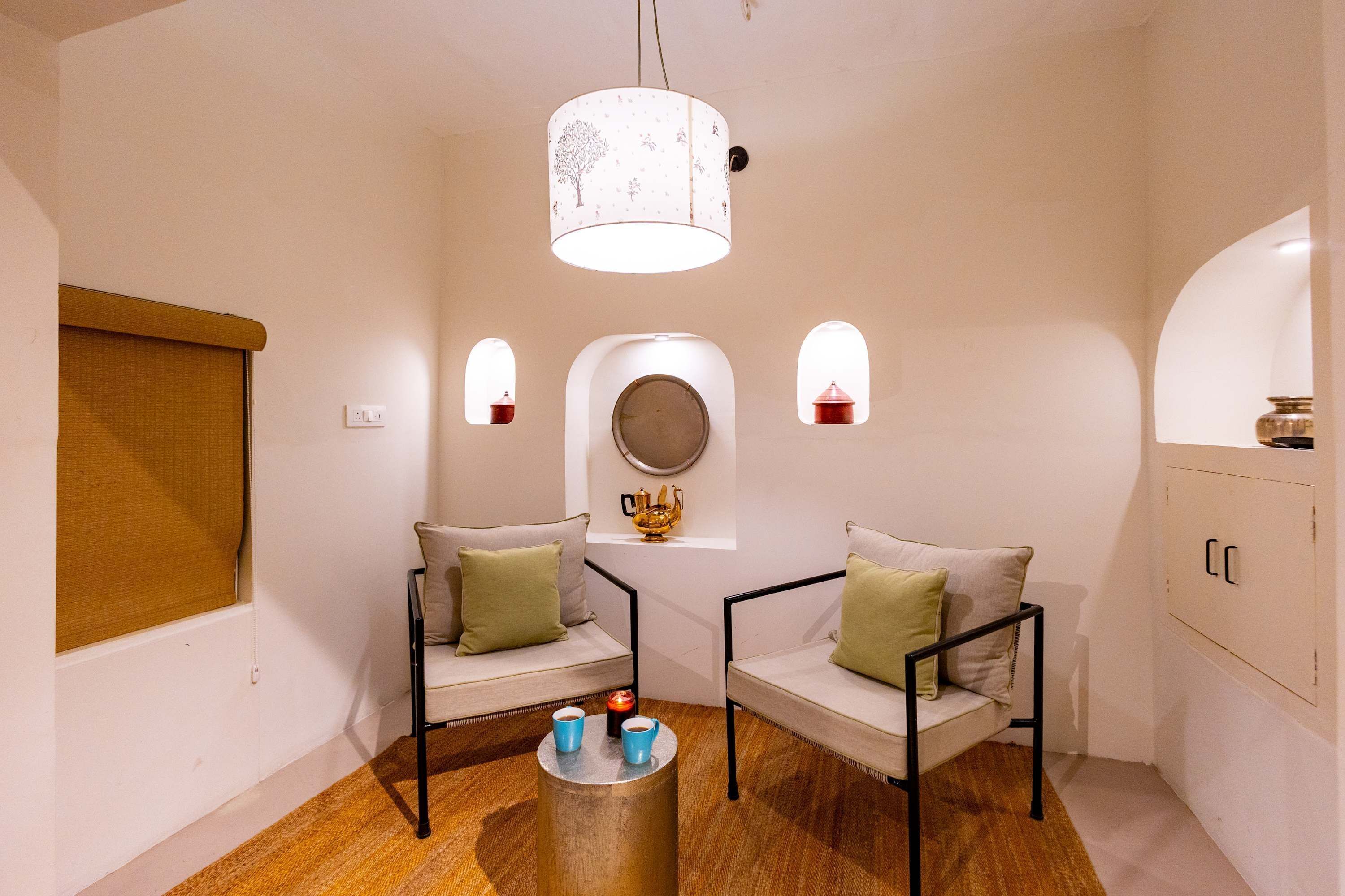 A room with two chairs, a round table with cups, a candle, and a hanging light fixture.