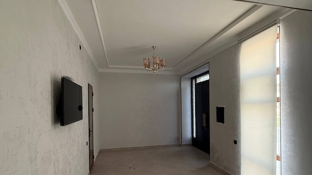 A spacious hallway with a flat ceiling, a mounted television, and a chandelier.