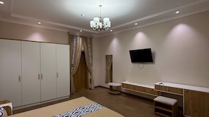 Un dormitorio con una cama grande, un televisor montado en la pared, un armario y un banco.