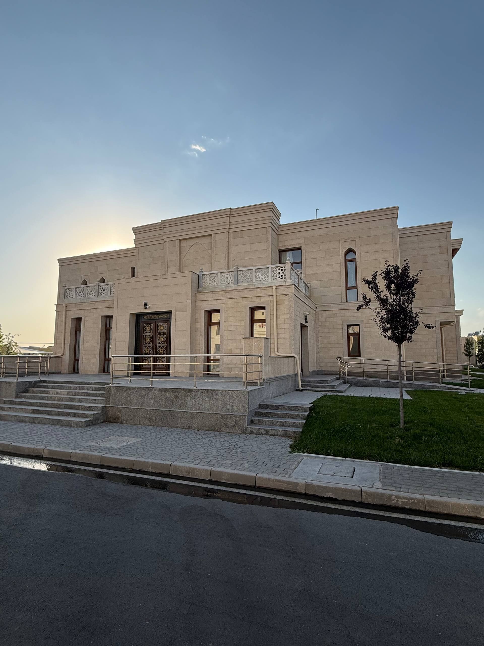 A modern building with a flat roof, a central entrance with a decorative door, and a small balcony with intricate railings.