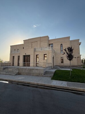 Un edificio moderno con techo plano, entrada central con puerta decorativa y un pequeño balcón con barandilla ornamentada.