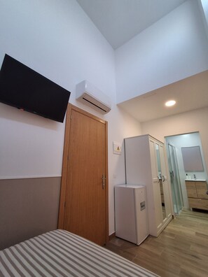 A hotel room with a bed, a wardrobe, a small refrigerator, an air conditioning unit, and a mirror.