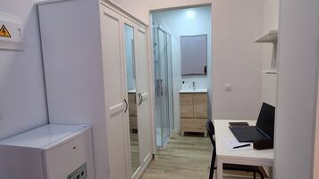 Een kleine kamer met een witte garderobe, een klein tafeltje met een laptop erop en een spiegel aan de muur.
