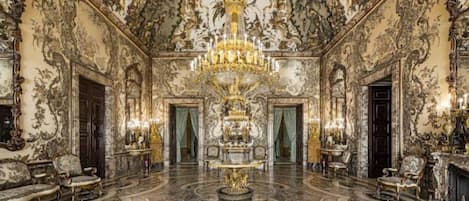 A grand room with ornate decorations, a large chandelier, and a central fireplace.