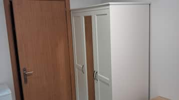 A room with a wooden door, a white wardrobe with two doors, and a small wooden shelf.
