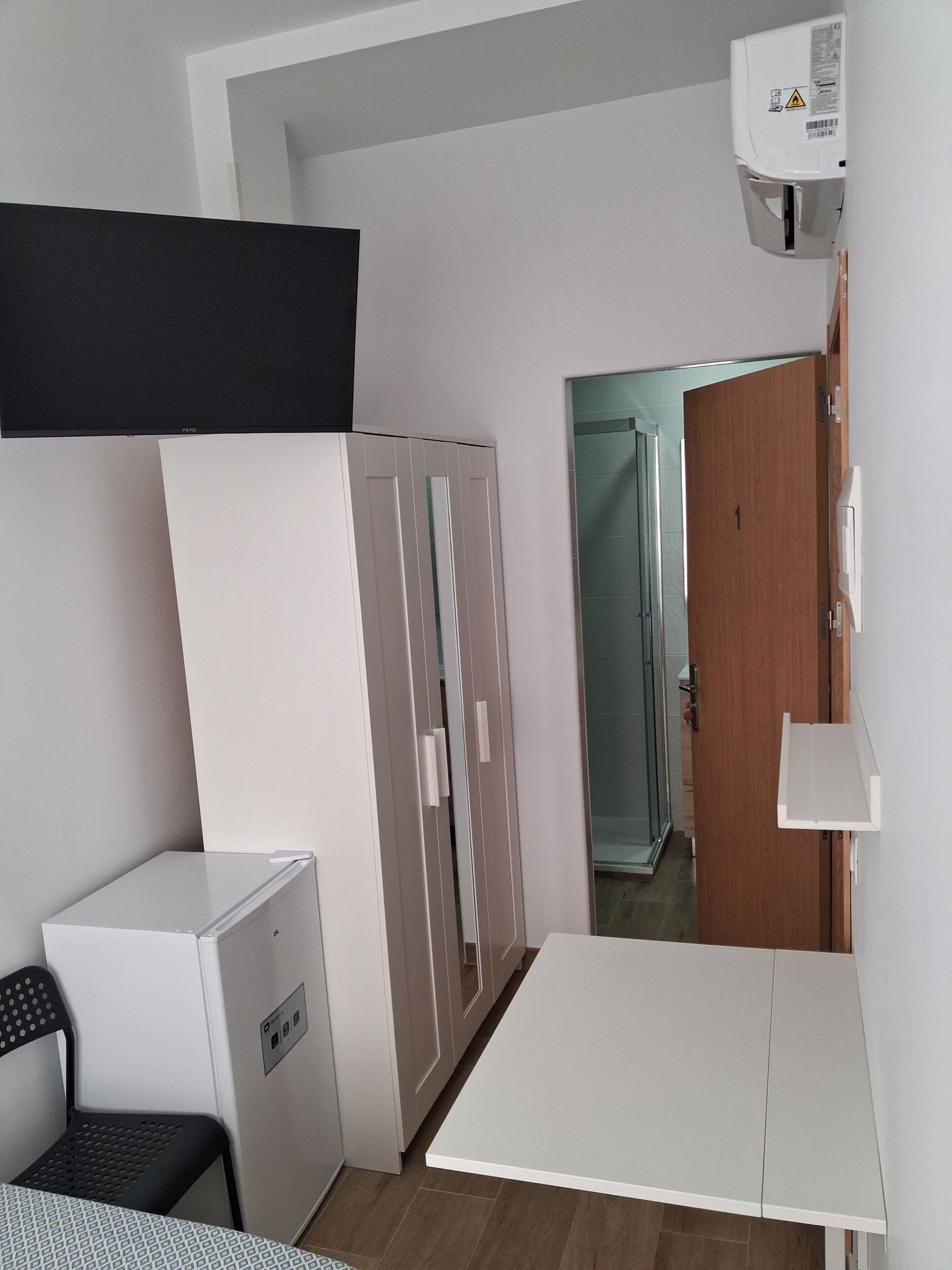 A compact room with a kitchenette, a wardrobe, a door leading to another room, and a white table.