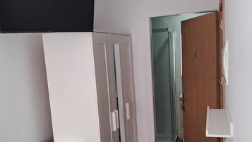 A compact room with a kitchenette, a wardrobe, a door leading to another room, and a white table.