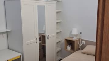 Een slaapkamer met een bed, een kledingkast met deuren, een nachtkastje met lamp en een klein plankje.