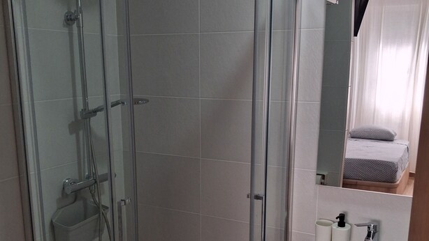 A modern bathroom with a glass-enclosed shower, a sink with a mirror, and a wooden cabinet. - House Amara y Pablo (Madrid)