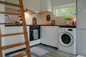 A compact kitchen with white cabinets, a built-in oven, a washing machine, and a window above the sink. - Cottage by Lake Bolmen (Bredaryd)
