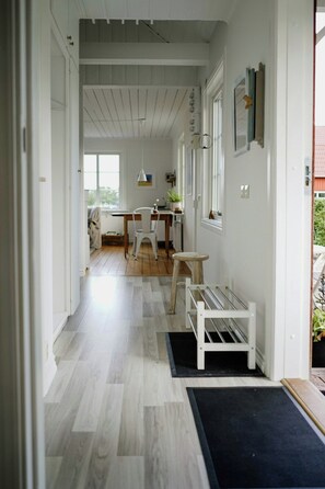A hallway with a wooden floor, a white bench, and a door leading to a room. - Cottage by Lake Bolmen (Bredaryd)