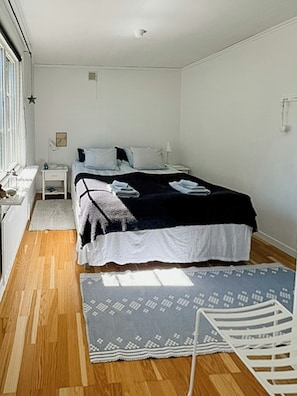 Un dormitorio con cama, mesitas de noche, una ventana y una alfombra estampada.