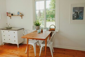 Un comedor con una mesa de madera, sillas blancas, un aparador blanco y una ventana con vistas a zonas verdes.