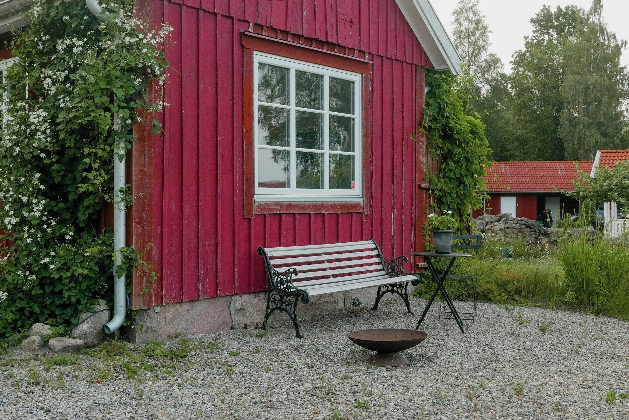A red wooden building with a white window, a bench, and a table with a bowl.