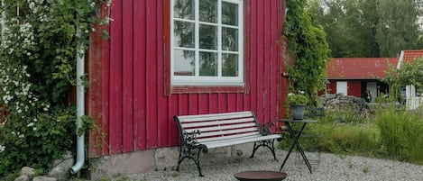 A red wooden building with a white window, a bench, and a table with a bowl.