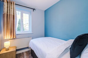 Ein Schlafzimmer mit Bett, einem Fenster mit Vorhängen, einem Heizkörper und einem Nachttisch mit Lampe.