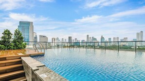 A rooftop infinity pool with a city skyline view, a wooden deck, and a metal railing. - Brayen by Kozystay - Tebet (South Jakarta)