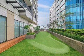 A modern building with a rooftop garden featuring artificial grass, planters with greenery, and a wooden deck. - Brayen by Kozystay - Tebet (South Jakarta)