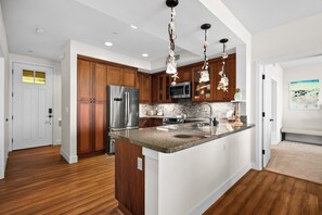 A modern kitchen with wooden cabinets, stainless steel appliances, and a granite countertop. - Pili Mai 6F by Alekona Kauai - 2BR Condo access to fitness (Koloa)