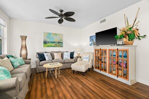 A living room with a sofa, armchair, coffee table, and a television on a cabinet. - Pili Mai 6F by Alekona Kauai - 2BR Condo access to fitness (Koloa)