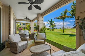 A spacious patio with wicker furniture, a ceiling fan, and a view of a well-maintained lawn and distant buildings. - Pili Mai 6F by Alekona Kauai - 2BR Condo access to fitness (Koloa)