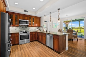 A modern kitchen with wooden cabinets, stainless steel appliances, and a large island. - Pili Mai 6F by Alekona Kauai - 2BR Condo access to fitness (Koloa)