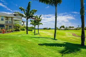 A well-maintained golf course with a clubhouse, palm trees, and a clear blue sky. - Pili Mai 6F by Alekona Kauai - 2BR Condo access to fitness (Koloa)
