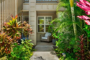 A narrow concrete pathway leading to a porch with a wicker sofa and a potted plant. - Pili Mai 6F by Alekona Kauai - 2BR Condo access to fitness (Koloa)