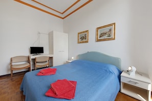 Ein Hotelzimmer mit einem Bett, einem Schreibtisch, einem Stuhl, einem Kleiderschrank und zwei gerahmten Bildern an der Wand.