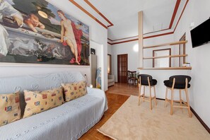 A living room with a sofa, patterned cushions, a painting, a TV, and a dining area with chairs and a table. - Casa Maderno: steps from the Lake (Toscolano Maderno)