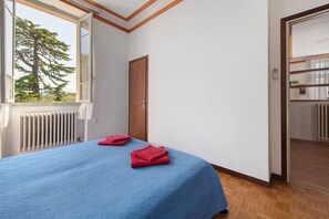 Ein Hotelzimmer mit Bett, Fenster mit Blick auf Bäume, Heizkörper und einer Tür zu einem Badezimmer.