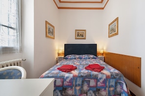 A hotel room with a bed, two bedside lamps, a window with curtains, and three framed pictures on the wall. - Casa Maderno: steps from the Lake (Toscolano Maderno)