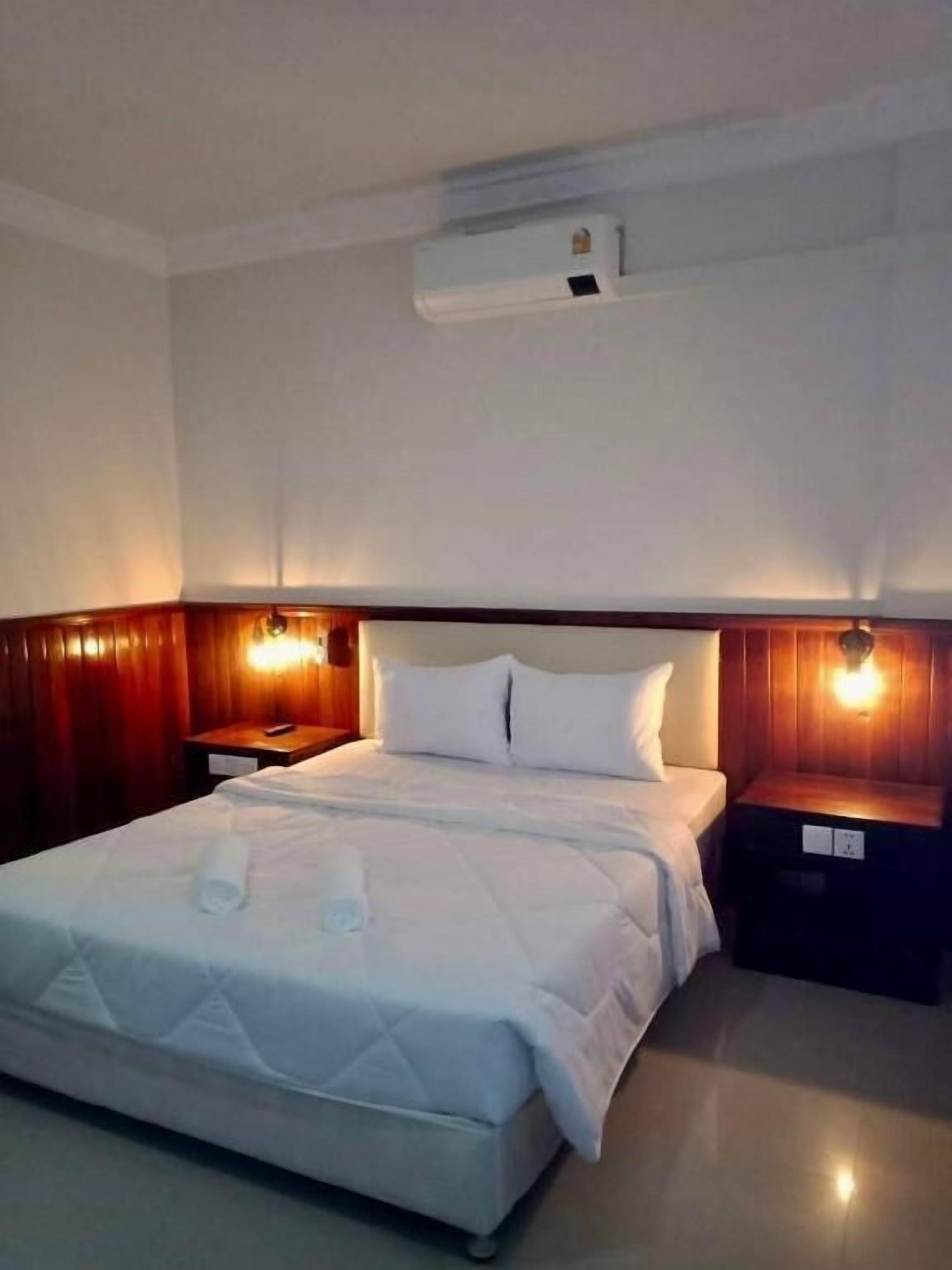 A hotel room with a bed, bedside tables, and an air conditioning unit.