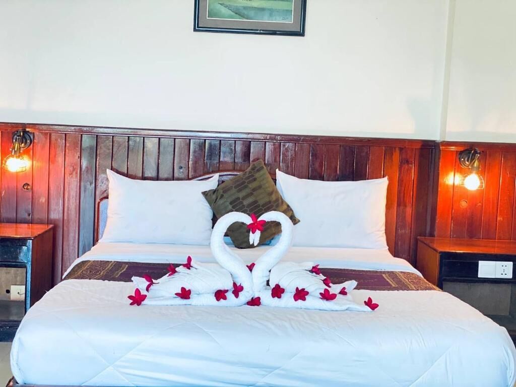 A hotel room with a bed, a wooden headboard, two bedside tables, and a wall-mounted light fixture.