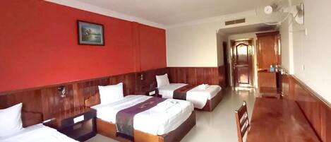 Habitación de hotel con dos camas, cabecera de madera, pared de acento roja, un cuadro enmarco y un ventilador.