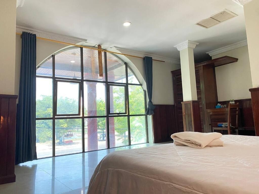 A hotel room with a large arched window, a bed with a neatly folded blanket, and a wooden wardrobe.