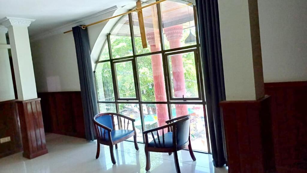 Una habitación con dos sillas de madera, un ventanal con vistas a follaje y un pilar de madera.